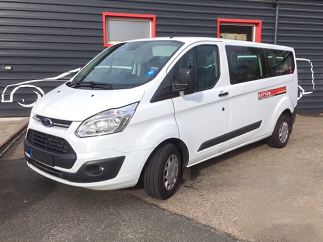 Weißer Ford Transit Kleinbus der Autovermietung Ritter vor einem Firmengebäude.