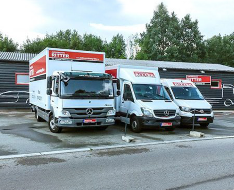 Drei weiße Mercedes-Benz Transporter und LKW der Autovermietung Ritter auf einem Parkplatz.
