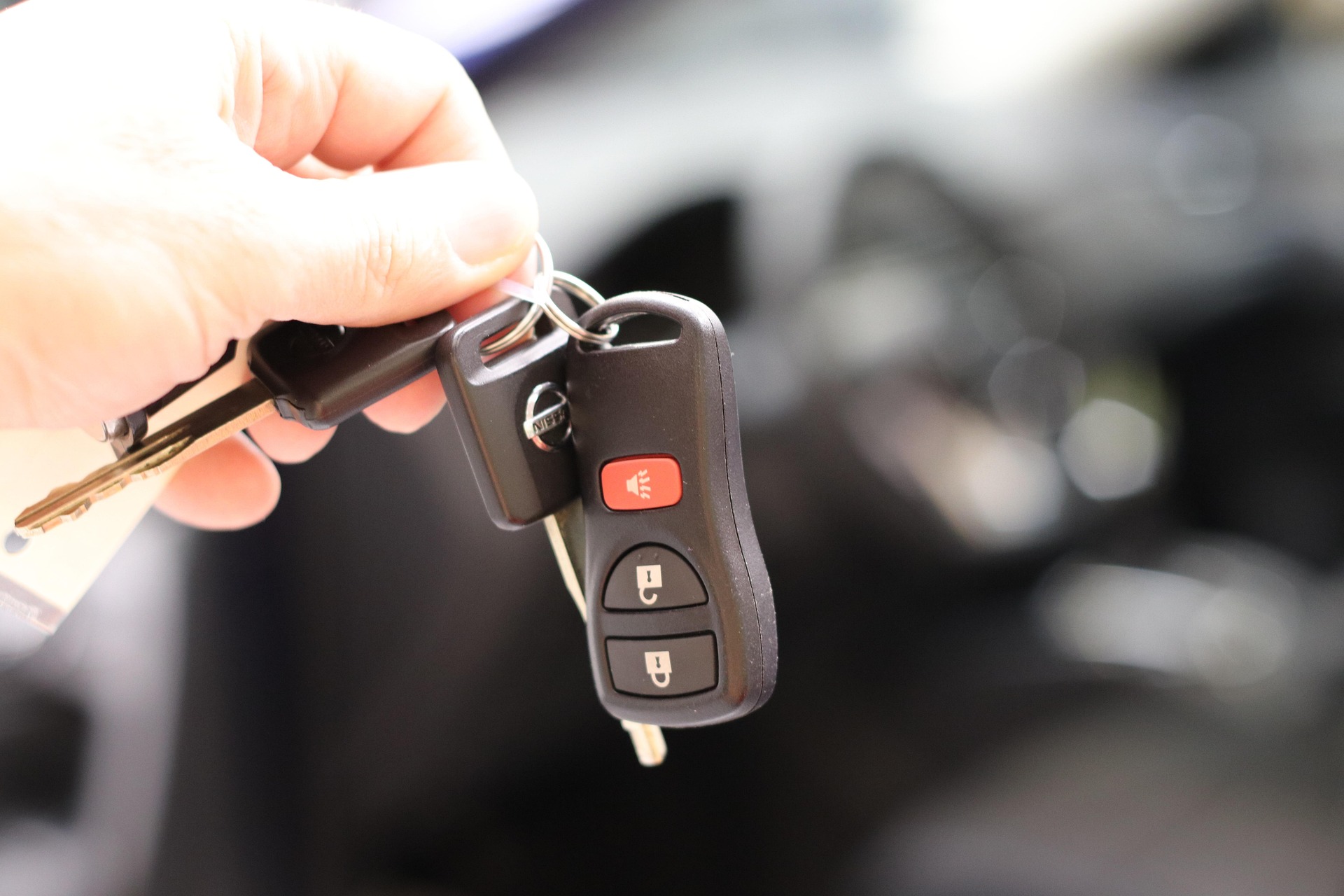 Hand hält Autoschlüssel vor unscharfem Fahrzeuginnenraum als Symbol für Fahrzeugverkauf.