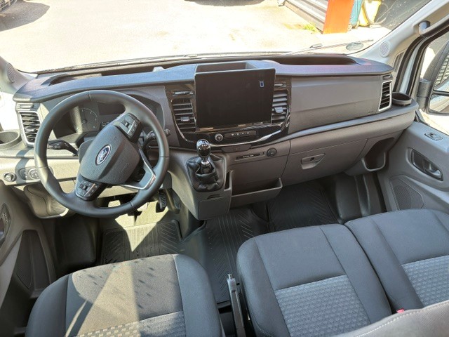 Cockpit eines Ford Kleinbusses mit Lenkrad, Armaturenbrett, Display und vorderen Sitzen.