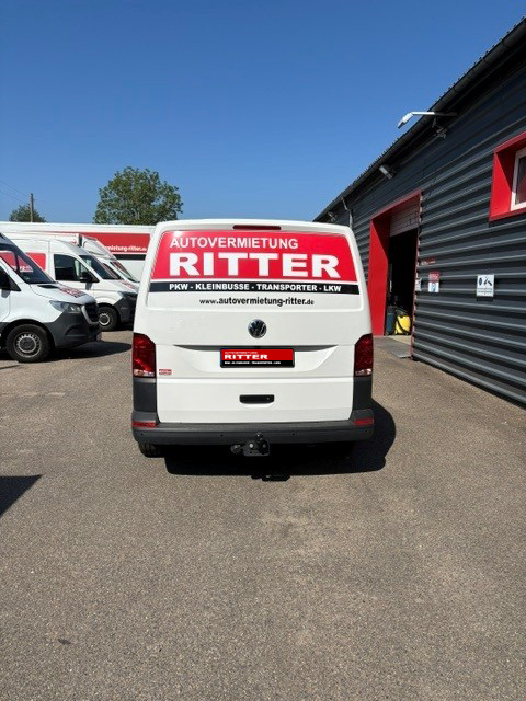 Heckansicht eines weißen VW Transporters der Autovermietung Ritter vor dem Firmengebäude.