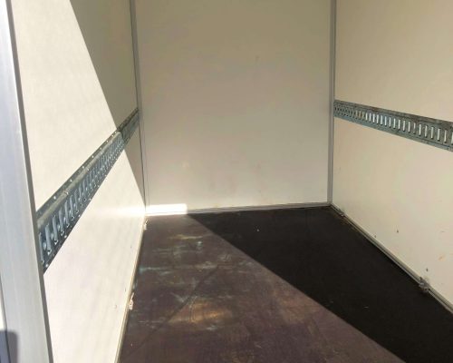 Innenraum eines Kofferanhängers mit leerer Ladefläche und seitlichen Befestigungsschienen.