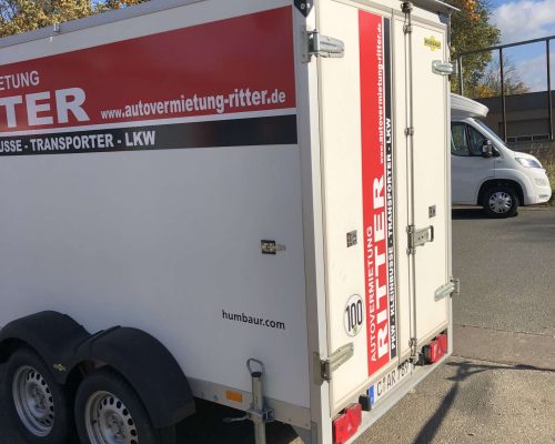 Weißer Kofferanhänger der Autovermietung Ritter in schräger Heckansicht.