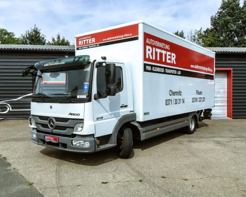Weißer Mercedes LKW der Autovermietung Ritter mit Kofferaufbau vor einem Firmengebäude.