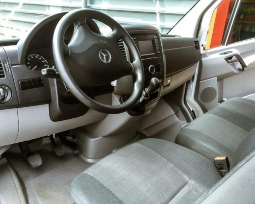 Cockpit eines Mercedes Transporters mit Lenkrad, Armaturenbrett und Sitzbank.