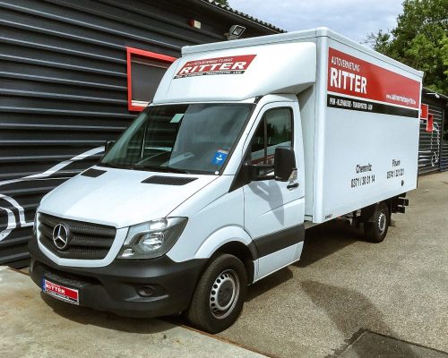 Weißer Mercedes LKW mit Kofferaufbau der Autovermietung Ritter vor einem Firmengebäude.