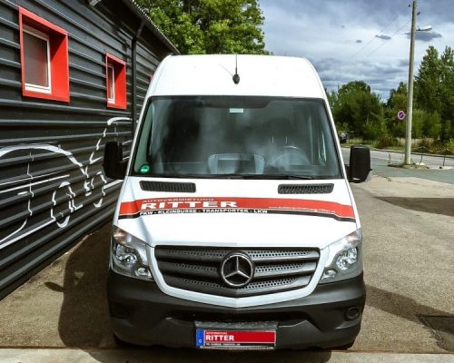 Weißer Mercedes Sprinter Transporter der Autovermietung Ritter vor einem Firmengebäude.