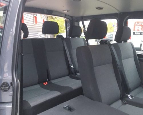 Innenraum eines VW T6 Kleinbusses mit mehreren Sitzreihen und Sicherheitsgurten.