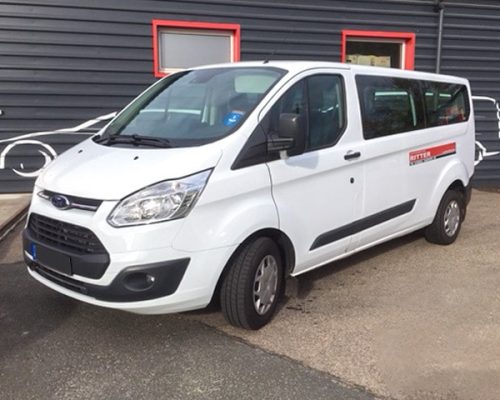 Weißer Ford Transit Kleinbus der Autovermietung Ritter vor einem Firmengebäude.
