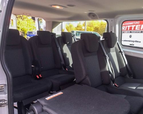Innenraum eines Kleinbusses mit mehreren Sitzreihen und Ritter-Fahrzeug im Hintergrund.