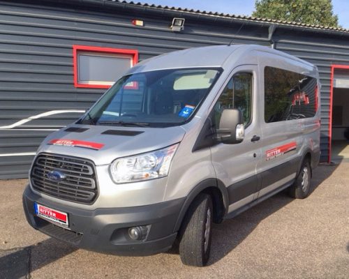 Silberner Ford Transit Kleinbus der Autovermietung Ritter vor einem Firmengebäude.
